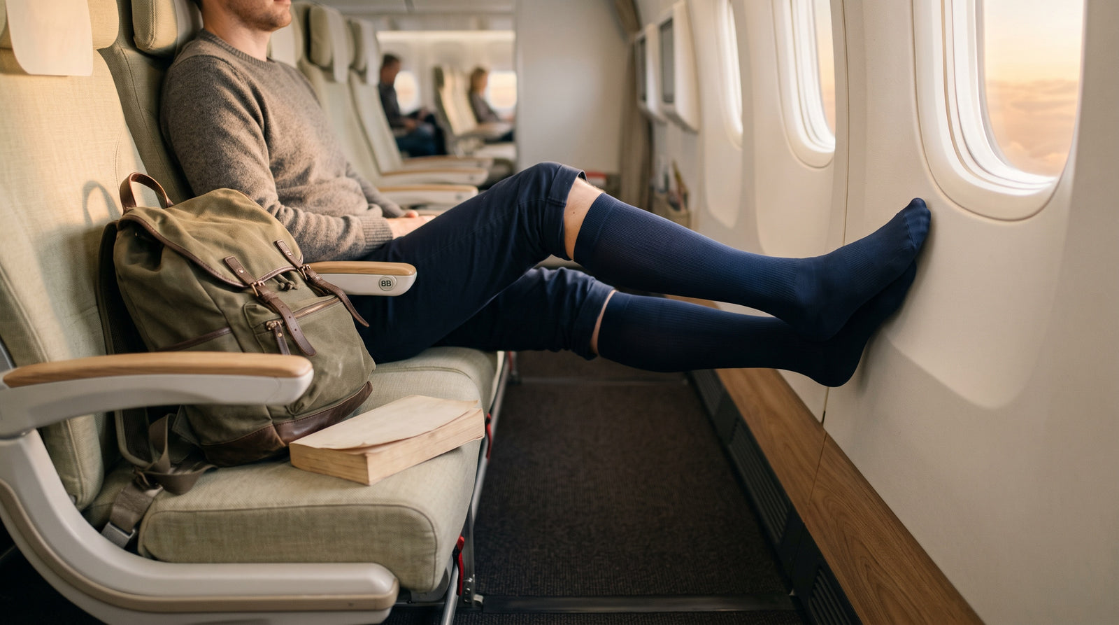 Junger Reisender im Flugzeug mit Kompressionskniestrümpfen und Rucksack am Fensterplatz